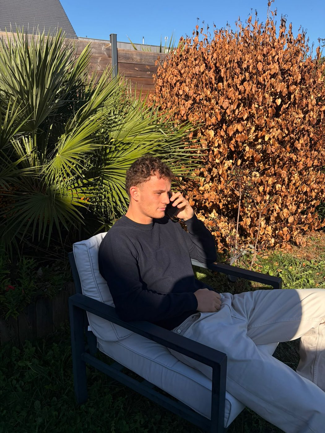 Thomas Lairy au téléphone, assis dans un jardin